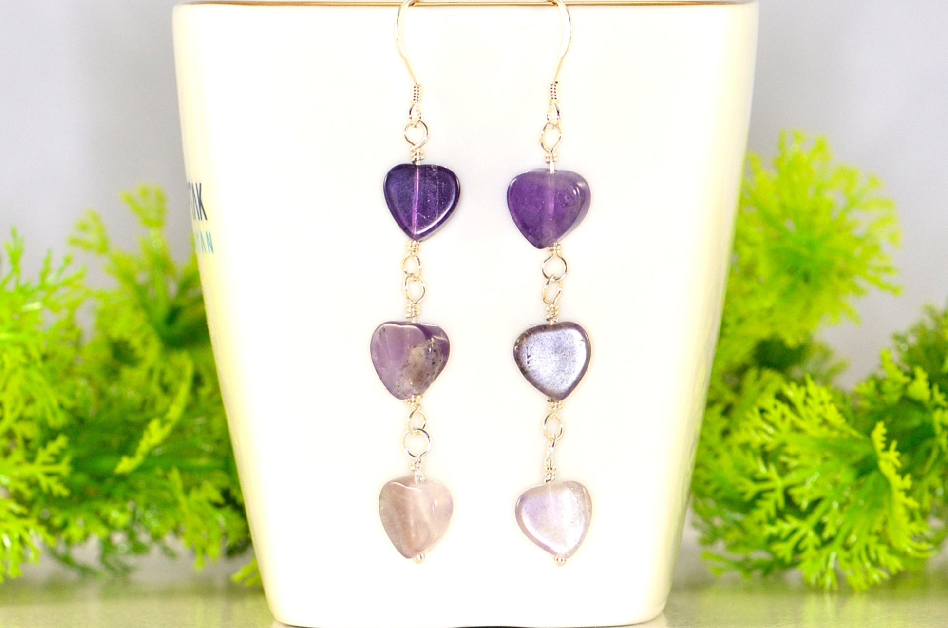 Natural Amethyst Heart Dangle Earrings displayed on a tea cup.