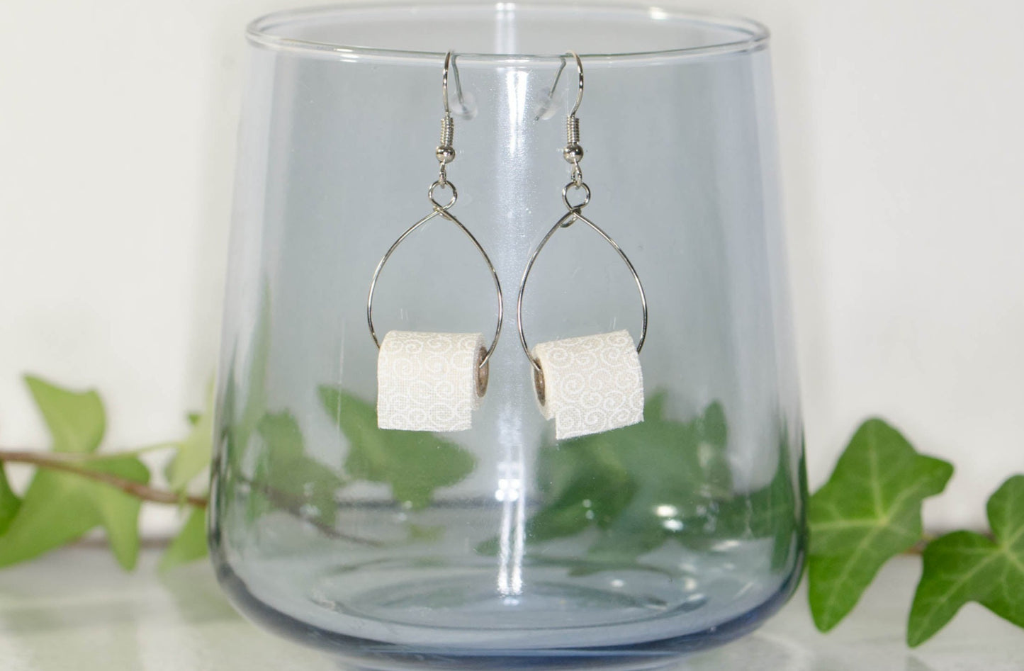 Miniature Toilet Paper Roll Earrings displayed on a glass.