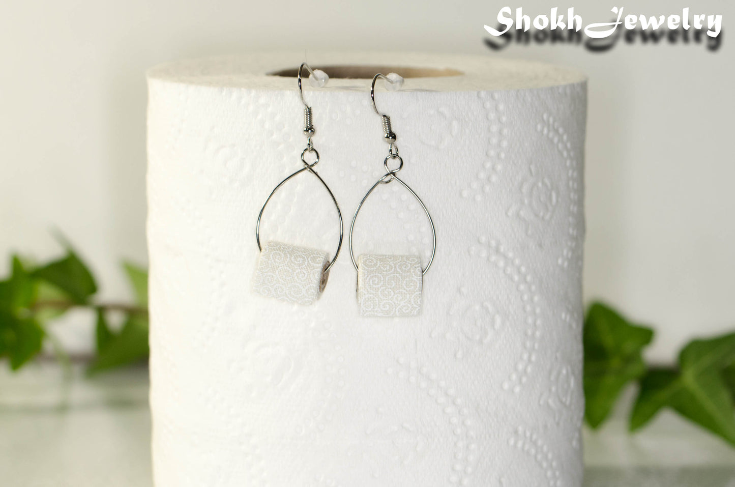 Tiny Toilet Paper Roll Earrings displayed on a toilet paper roll.