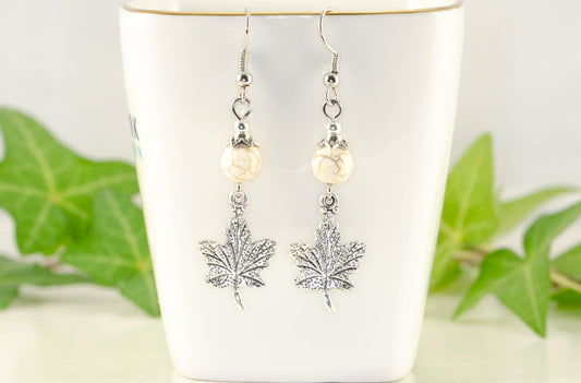 White Howlite and Tibetan Silver Maple Leaf Dangle Earrings displayed on a tea cup.