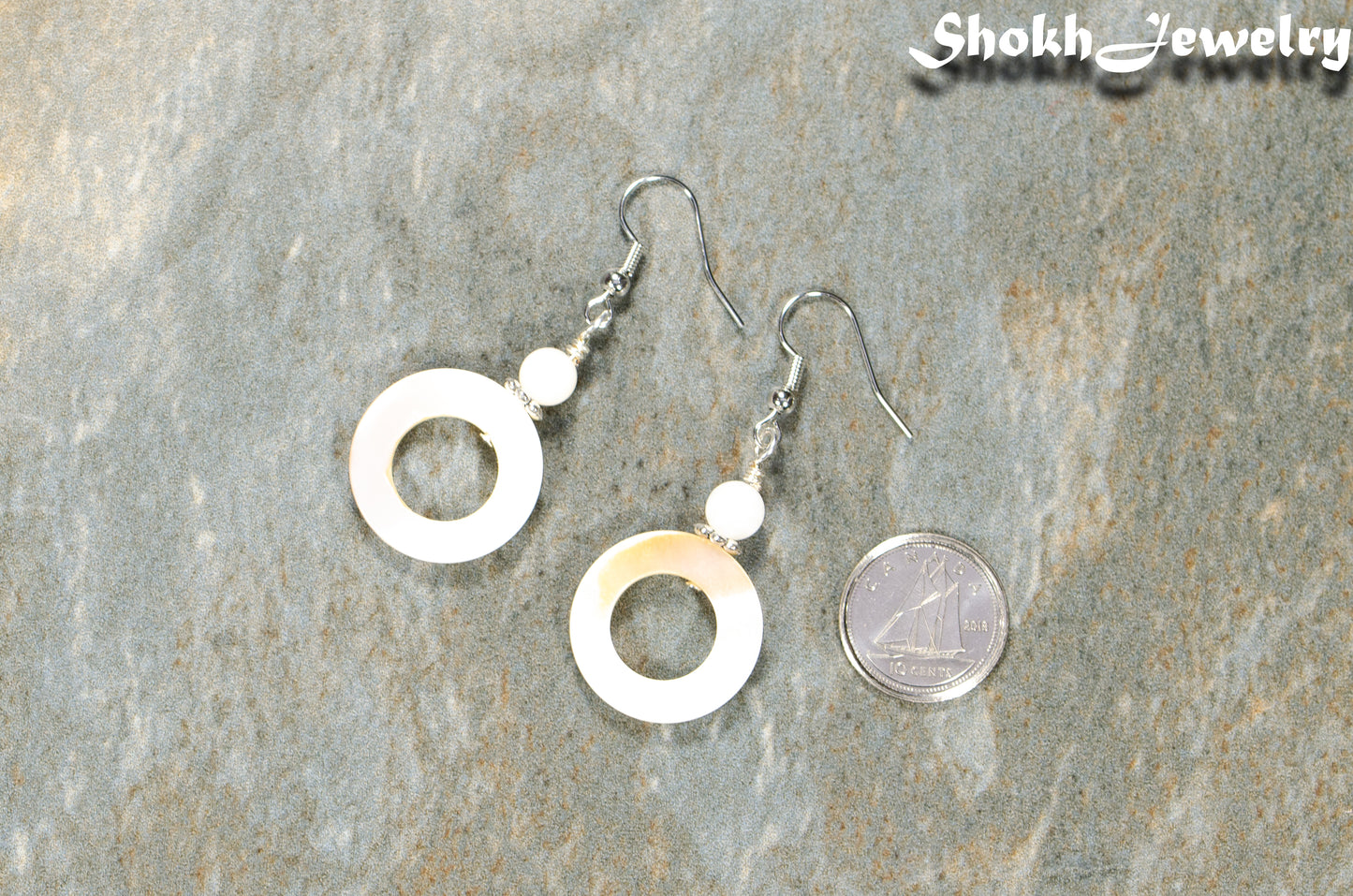 White Doughnut Seashell Earrings beside a dime.