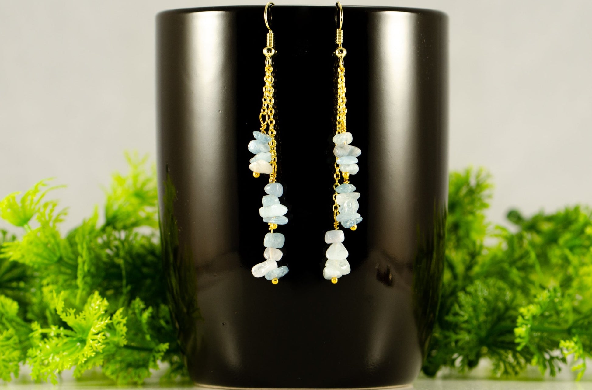 Long Gold Plated Chain and Aquamarine Crystal Chip Earrings on a coffee mug.