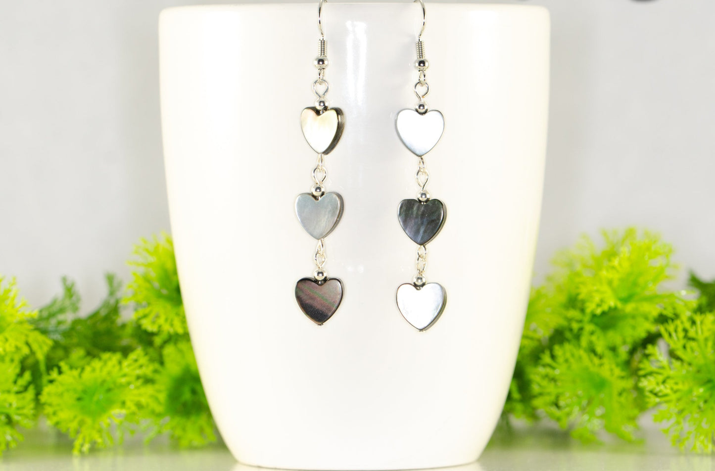 Long Grey Seashell Hearts Earrings displayed on a coffee mug.