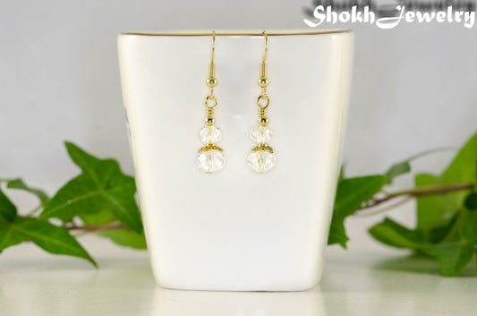 Gold earrings with clear beads on a white cup against a light background