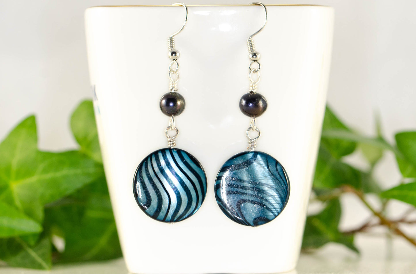Long Blue Seashell and Pearl Earrings displayed on a tea cup.